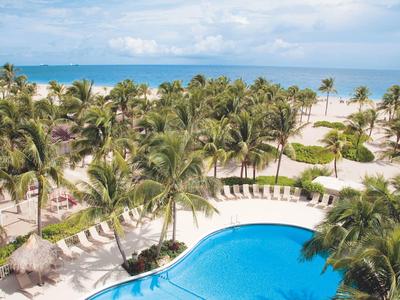 Beach resort with large pool, palm trees, and ocean view under blue sky.