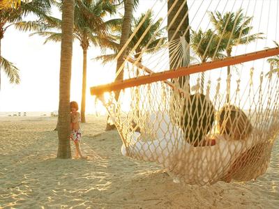 People relaxing in a hammock on a beach with palm trees at sunset.