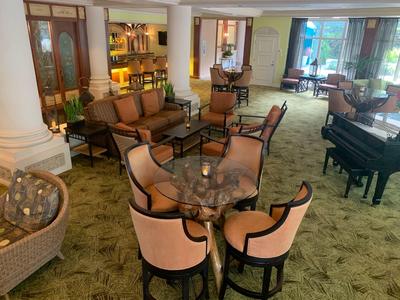 Cozy hotel lounge area with armchairs, tables, and grand piano near window.