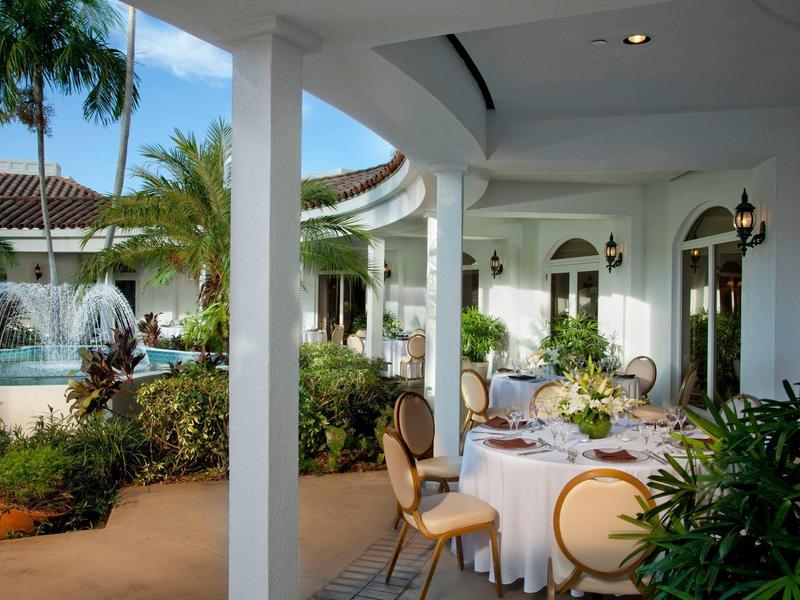 Elegant outdoor terrace restaurant with round tables and fountain in a tropical setting.
