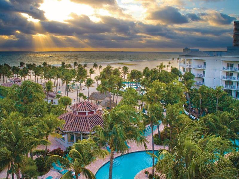 View of tropical resort with pool, palm trees, and sea at sunset.