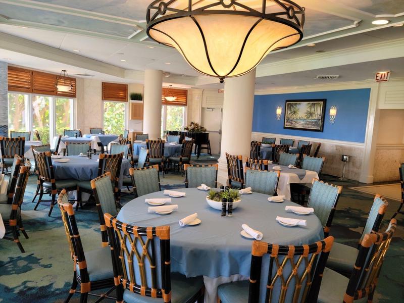 Hotel dining room with round tables, blue tablecloths, wooden chairs, and a large ceiling light fixture