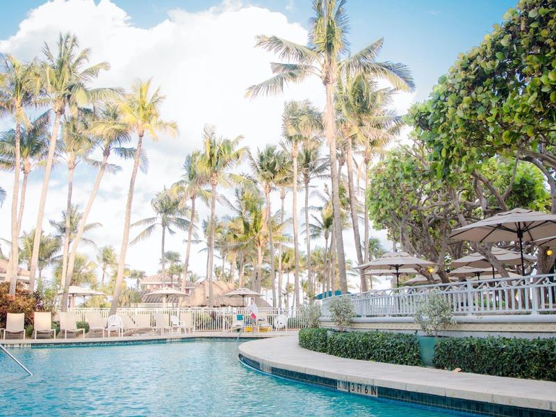 Pool area with lounge chairs and palm trees in a tropical hotel resort.