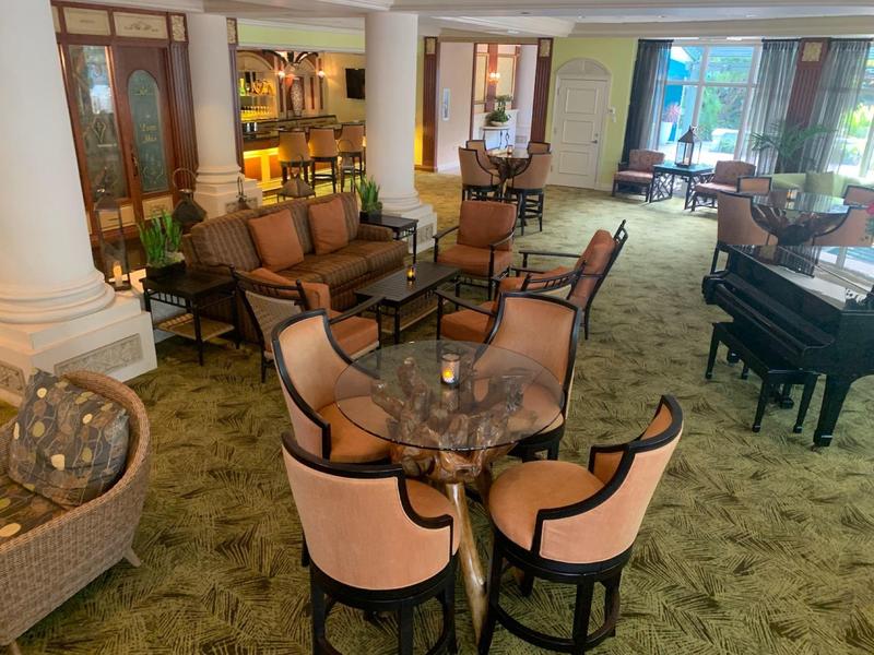 Cozy hotel lounge area with armchairs, tables, and grand piano near window.