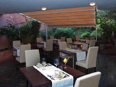 Moderner Außenbereich mit gedeckten Tischen, beigen Stühlen, Holzdecke und grüner Pflanzenwand.