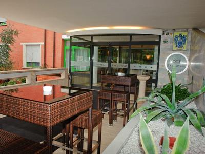 Überdachte Terrasse mit braunen Holztischen und Stühlen, Pflanzen und Glasvitrine im Hintergrund.