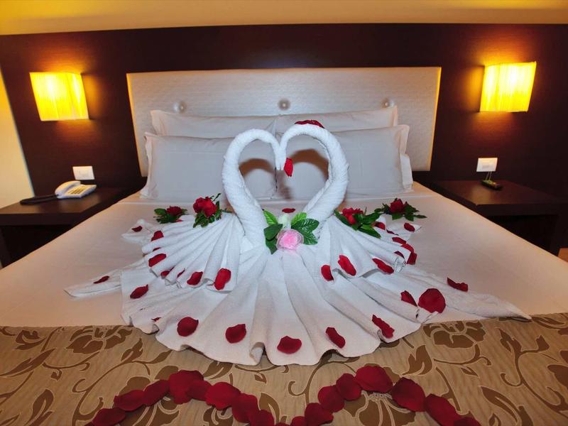 Ein Doppelbett mit weißen Tüchern und Rosenblättern, dekoriert zu zwei Schwänen geformt, mit warmem Licht.