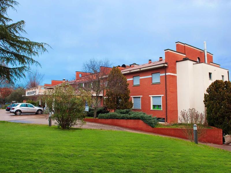 Mehrstöckiges rotes Backsteingebäude mit Parkplätzen und grünem Rasen im Vordergrund.