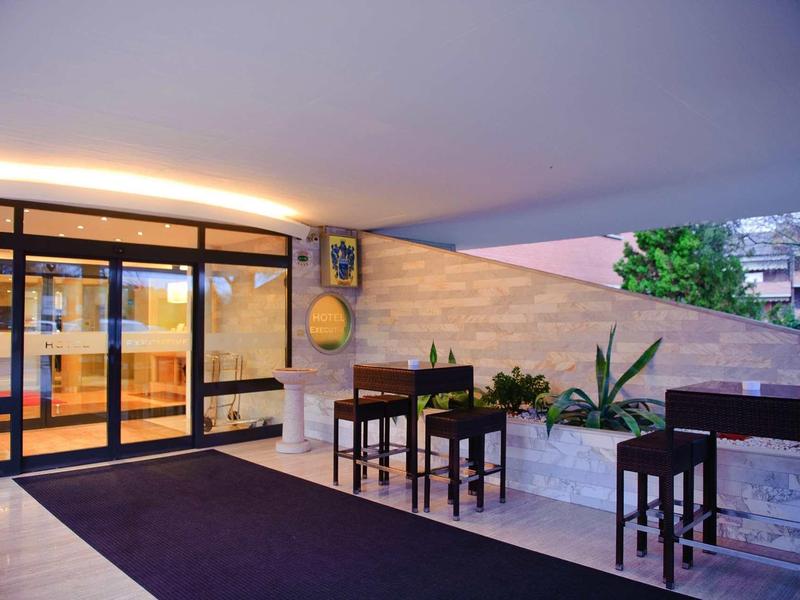 Eingangsbereich mit Glas-Schiebetür, Gartentisch mit Stühlen und Pflanzen vor heller Steinwand.