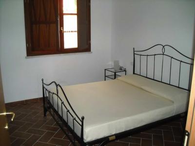 Ein einfaches Schlafzimmer mit Metallbett, nach unten geöffnetem Fenster und kleinem Nachttisch.