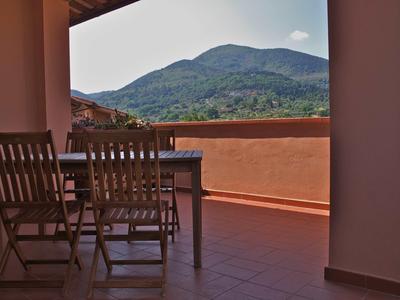 Balkon mit Holztisch und Stühlen, bergige Landschaft im Hintergrund unter blauem Himmel.
