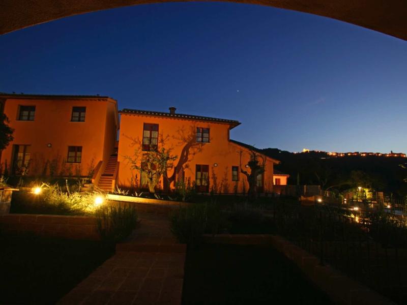 Ein Gebäude in sanftem Abendlicht, klarer Himmel, mit beleuchtetem Gartenweg und Hügel im Hintergrund.