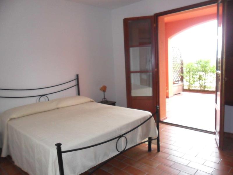 Schlichtes Schlafzimmer mit Metallbett und offenem Glastür zur Terrasse mit viel Tageslicht.