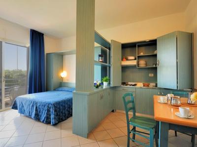 Gemütlicher Wohnraum mit Schlafbereich, blauen Vorhängen, Kleiderschrank, Esstisch und Stühlen.