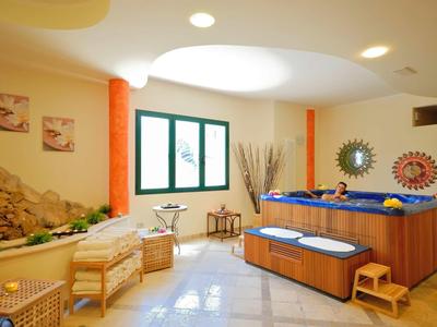 Innenraum mit Whirlpool, zwei Stühlen, Fenstern und dekorativem Sonnen- und Mondspiegel an der Wand.