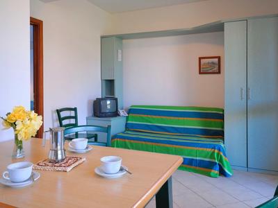 Ein heller Raum mit einem Tisch, gedeckt mit Tassen und Blumen, und einer grünen Couch mit TV.