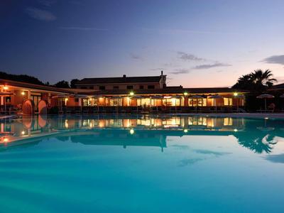 Beleuchteter Hotelpool bei Abenddämmerung mit reflektierenden Wasseroberflächen und Palmen.