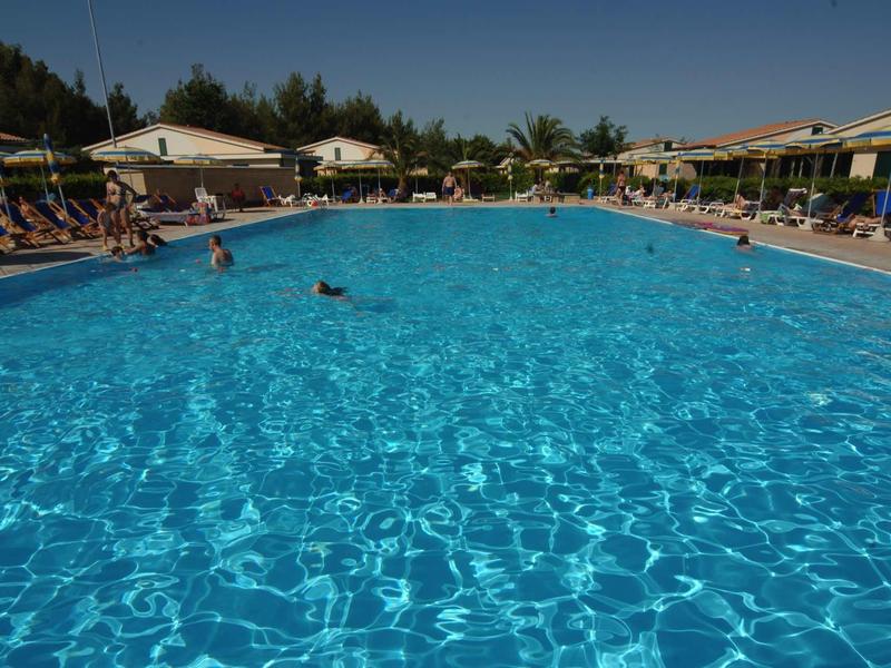 Großes rechteckiges Schwimmbecken mit klarem blauem Wasser, umgeben von Liegestühlen und Sonnenschirmen.