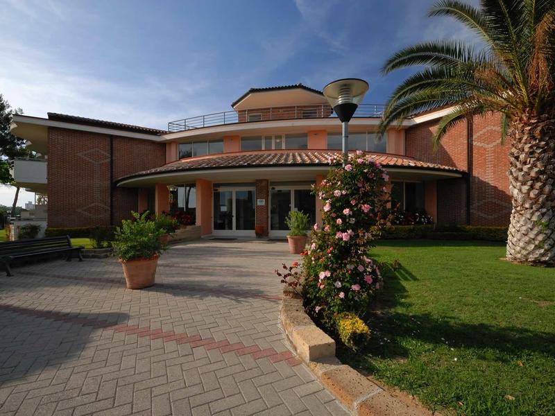 Ein großes Gebäude mit rotem Ziegeldach, umgeben von Grünflächen, Palmen und Blumen.