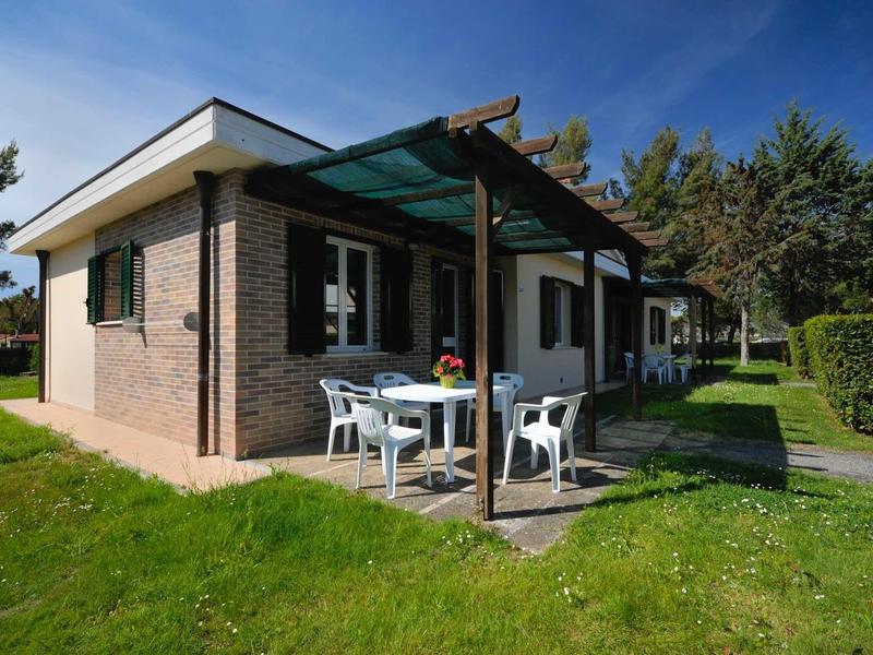 Einfamilienhaus mit braunem Ziegelmauerwerk, grünem Sonnenschutz und weißem Gartentisch mit Stühlen.