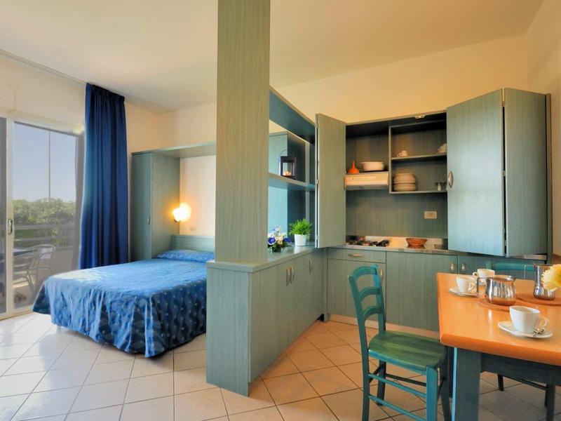 Gemütlicher Wohnraum mit Schlafbereich, blauen Vorhängen, Kleiderschrank, Esstisch und Stühlen.