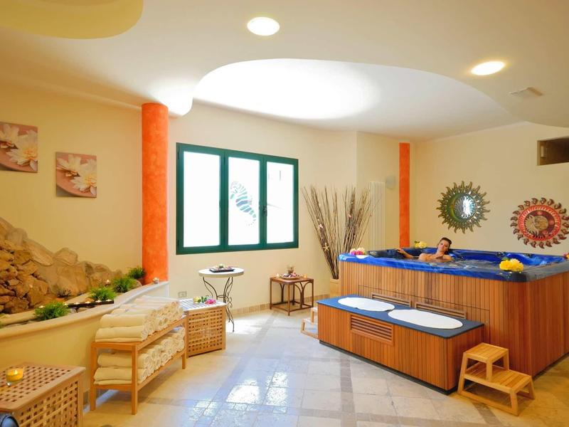 Innenraum mit Whirlpool, zwei Stühlen, Fenstern und dekorativem Sonnen- und Mondspiegel an der Wand.