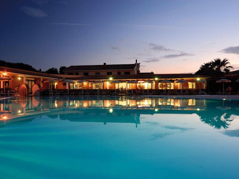 Großer beleuchteter Pool vor niedrigem Gebäude bei Dämmerung mit Reflexion im Wasser.