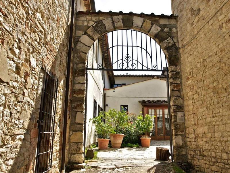 Enger Steinbogen zwischen alten gemauerten Häusern mit sonnigem Innenhof und Pflanzen.