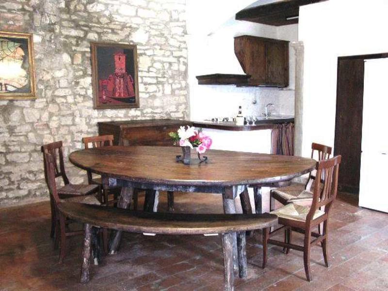 Rustikaler Essbereich mit runder Holztisch, Bank, Stühlen und Steinstückwand im Hintergrund.