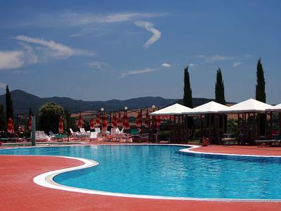 Großer blauer Pool mit roten Liegestühlen und weißen Sonnenschirmen, Berge im Hintergrund.