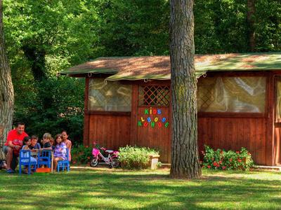 Dzieci siedzą na zewnątrz przy małym stoliku obok drewnianego domu w ogrodzie.