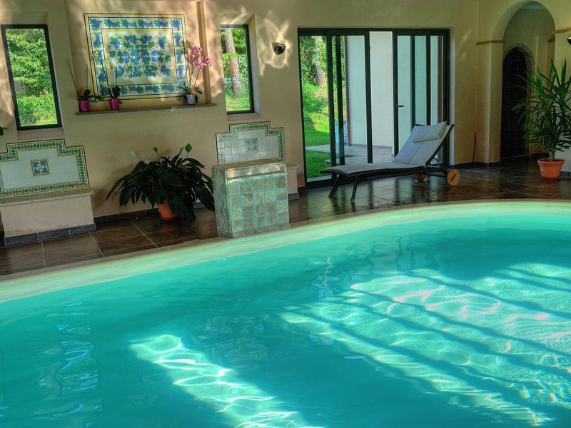 Basen kryty z leżakami i roślinami w jasnym, przytulnym pomieszczeniu.