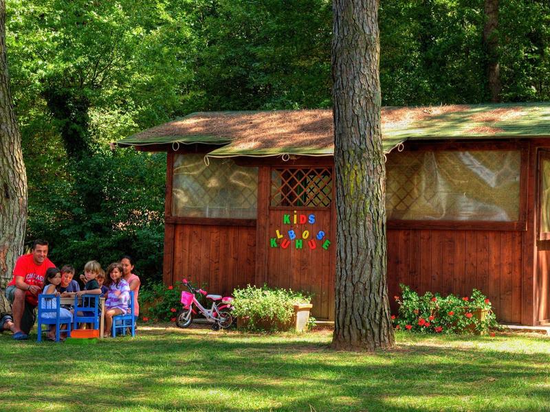 Dzieci siedzą na zewnątrz przy małym stoliku obok drewnianego domu w ogrodzie.