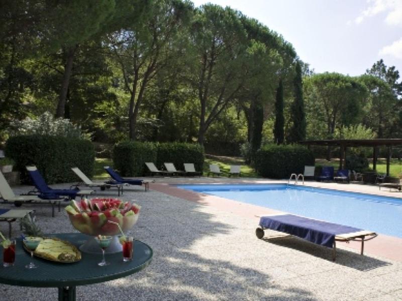 Strefa basenu z leżakami i stołem w ogrodzie hotelowym otoczonym drzewami.