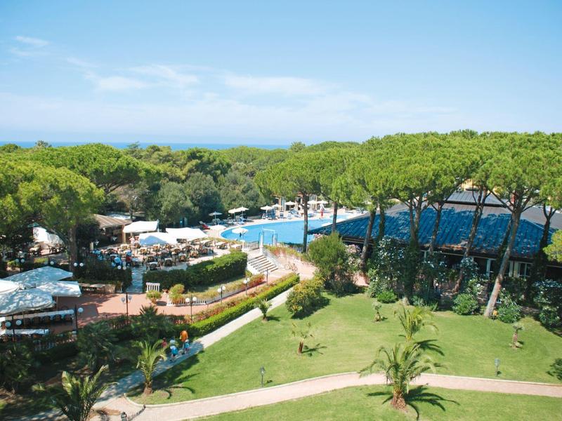 View of a pool area with sun loungers and green garden under a clear sky.
