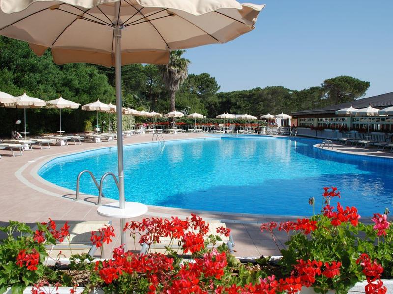 Large hotel pool with sun umbrellas and flowers in the foreground on a sunny day.