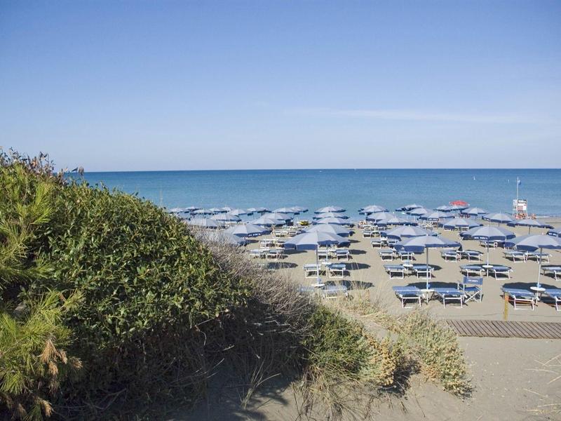 Beach with many blue umbrellas and view of calm sea under clear sky.