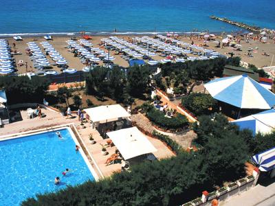 Vogelperspektive auf einen Strand mit Sonnenschirmen und einen Poolbereich neben einem Hotel.