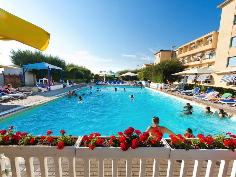 Druk zwembad buiten bij een hotel met ligstoelen en zwemmende mensen in daglicht.