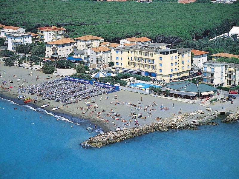 Strandhotel met ligstoelen, zandstrand en rotsen bij turquoise zee.