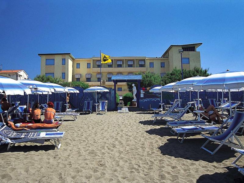 Strand met parasols en ligstoelen voor een groot hotelgebouw onder een blauwe lucht.