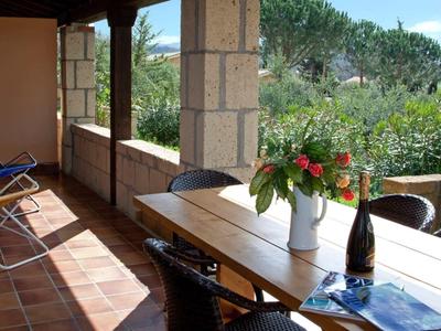 Überdachte Terrasse mit Holztisch, Stühlen, Flaschen, Blumen und Blick auf grünen Garten.