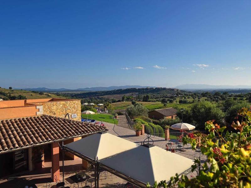 Landschaft mit Häusern, grünen Feldern und klarem blauem Himmel bei Sonnenlicht.