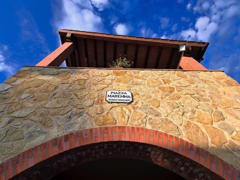 Haus mit Natursteinfassade, rotem Ziegelbogen und blauem Himmel mit Wolken im Hintergrund.