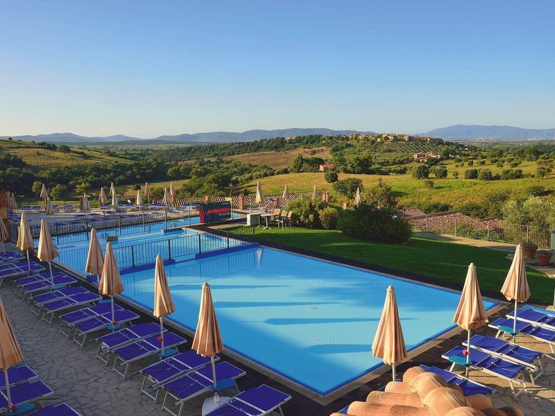 Großer rechteckiger Pool mit Liegestühlen und geschlossenen Sonnenschirmen in ländlicher Umgebung.