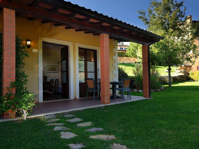 Haus mit Terrasse, rotem Holzüberdach, Rasen und Trittsteinen, umgeben von Bäumen und Sträuchern.