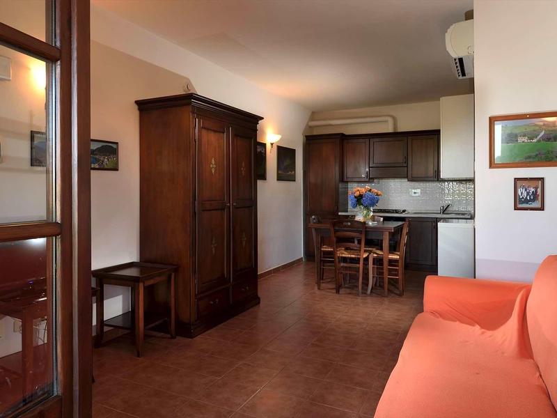 Gemütliches Wohnzimmer mit braunem Holzschrank, Esstisch, orangem Sofa und offener Küche.