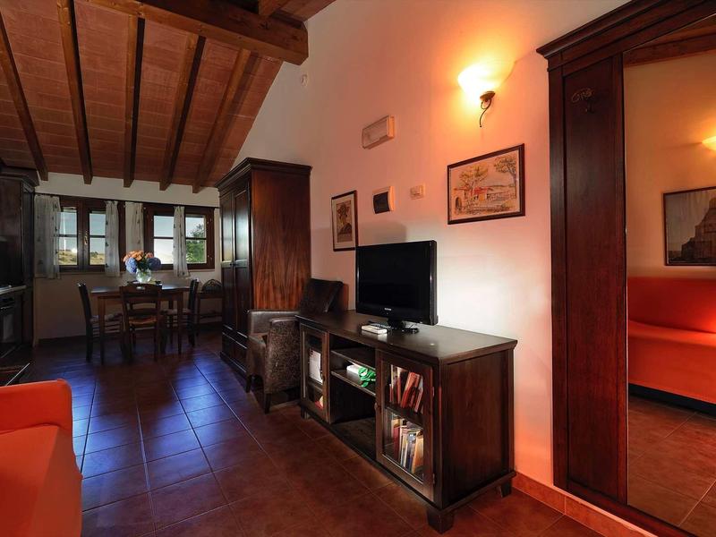 Wohnzimmer mit Holzdecke, dunklem Holzmobiliar, rotem Sofa und angrenzendem Schlafzimmer.