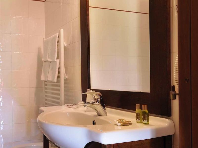 Kompaktes Badezimmer mit hellem Spiegel, weiße Keramikwaschbecken, Holzunterschrank und Handtücher.