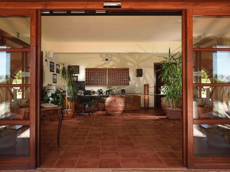 Weit geöffnete Holztüren führen in einen hellen Raum mit Pflanzen und rustikalem Steinboden.